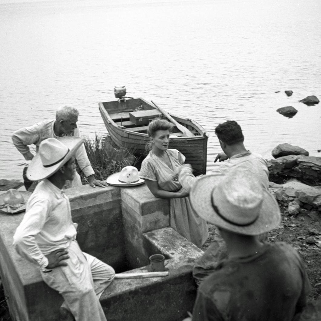 Esperanza Lopez Mateos talking to a group of men with boat and lake behind