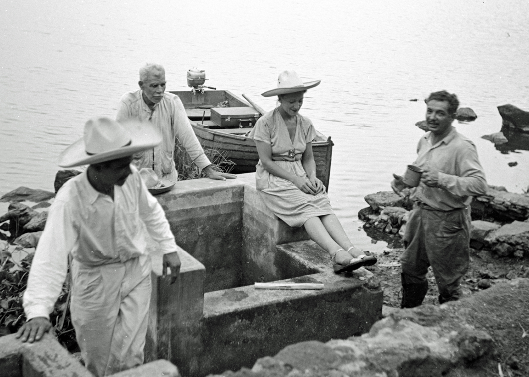 Esperanza Lopez Mateos talking to a group of men with boat and lake behind