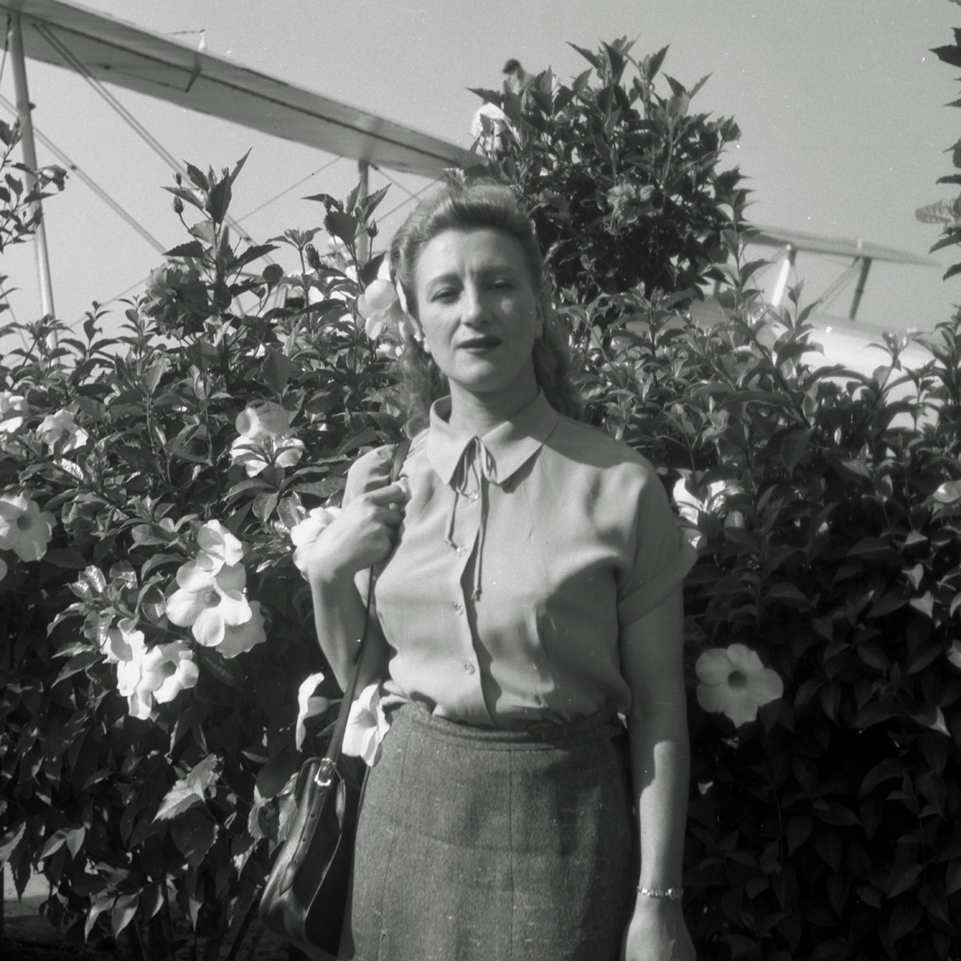 Esperanza standing in front of flowers with airplane behind