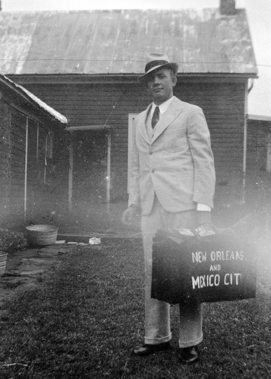 Henry standing with suit and suitcase in farmyard ready to travel